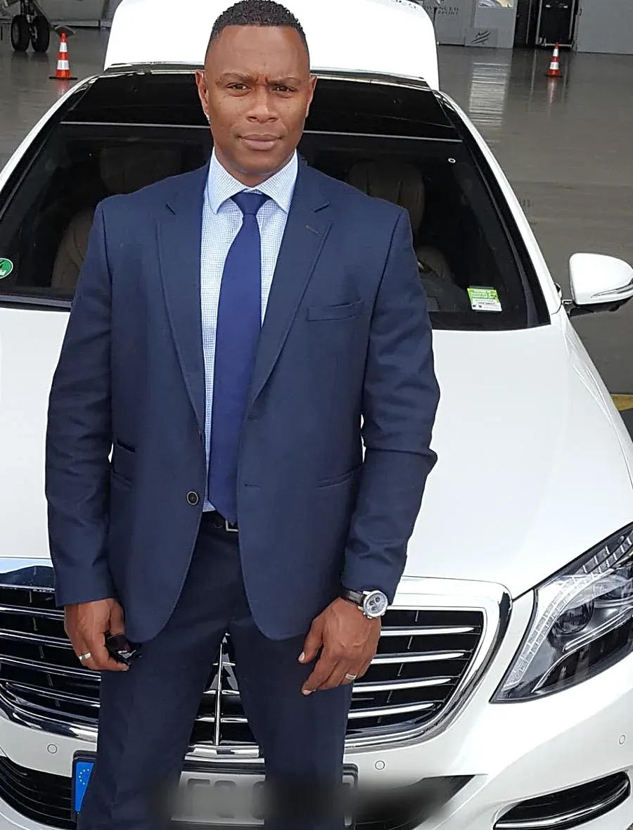 Chauffeur en costume devant la Mercedes Classe S sur le tarmac